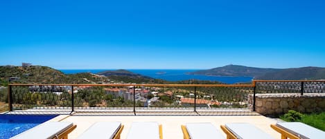 Un espace aménagé au bord de la piscine, avec des chaises longues et une vue sur la mer et les collines.