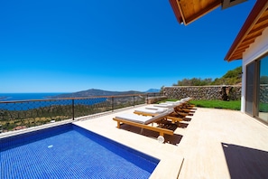 Área à beira da piscina com espreguiçadeiras e vista para o mar.