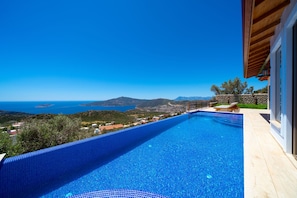 Piscina azul límpida com vista para o mar e montanhas.