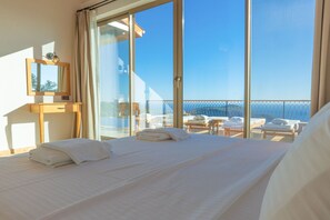 A hotel room with a large bed, a bedside table, a mirror, and a view of the sea through floor-to-ceiling windows. - Akasya Ena in Kalkan Belediyesi (Kaş)