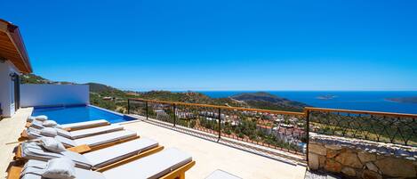 Ein Poolbereich mit Liegestühlen und Blick auf das Meer.