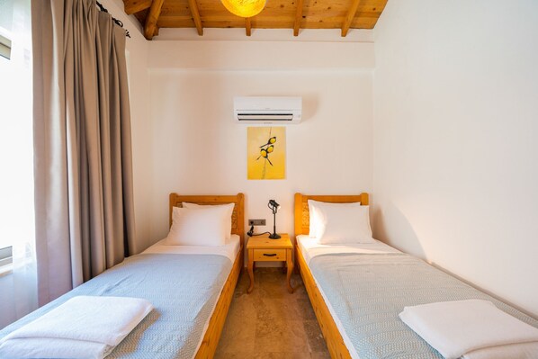 A room with two single beds, a wooden ceiling, an air conditioning unit, a nightstand with a lamp, and a painting on the wall. - Akasya Ena in Kalkan Belediyesi (Kaş)
