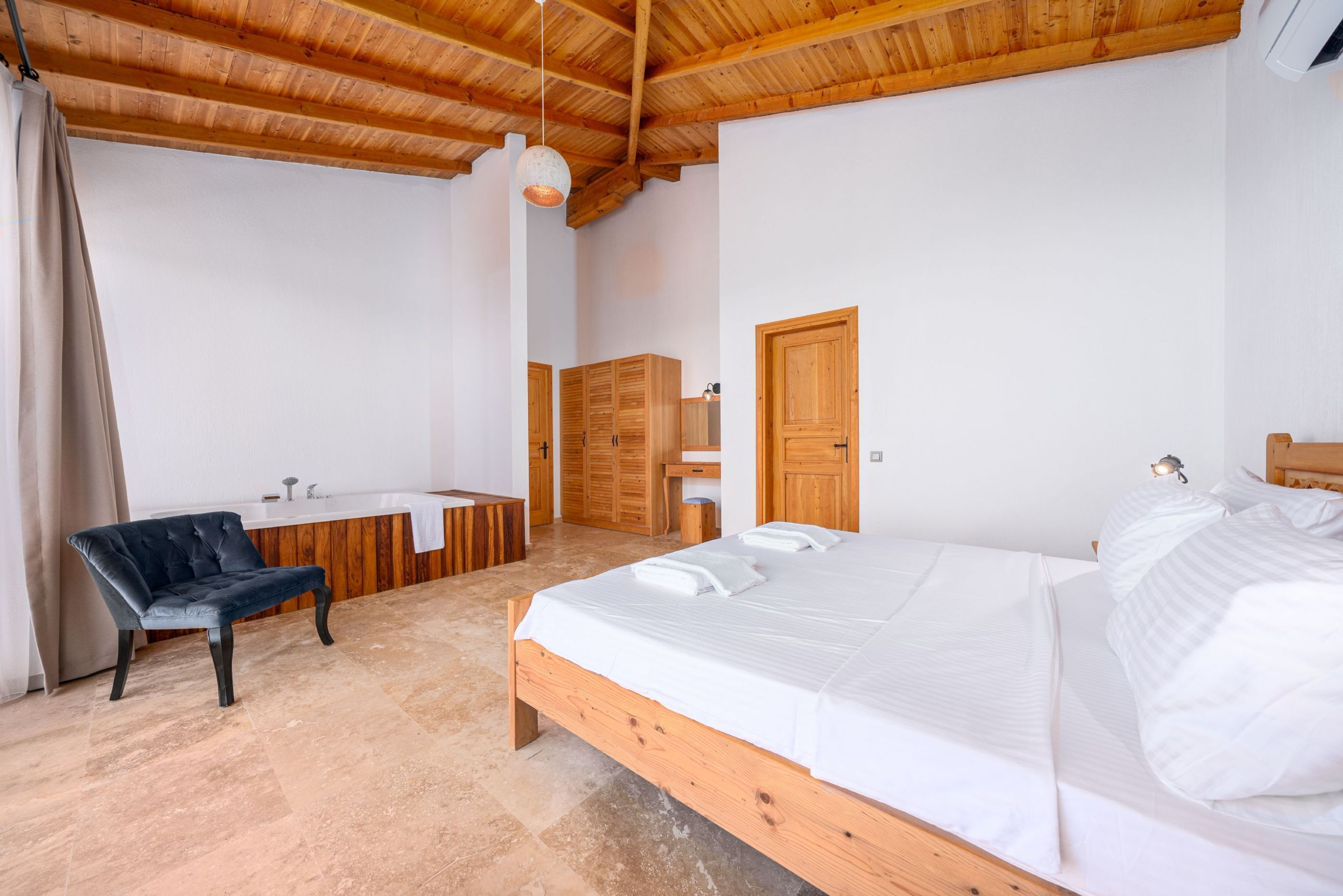 A bedroom with a wooden bed, a black leather chair, a wooden wardrobe, and a bathroom with a wooden vanity.