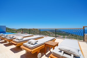 Uma área de lounge no terraço com espreguiçadeiras e vista para o mar.