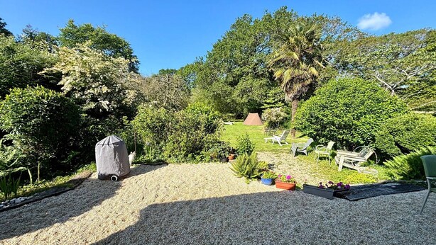 Ein Garten mit Kiesweg, Grillhaus und Gartenmöbeln.