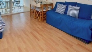 A living room with a blue sofa, striped blanket, and wooden floor. - Seaside studio with terrace, air conditioning and WIFI in Platja d'Aro (Platja d'Aro)