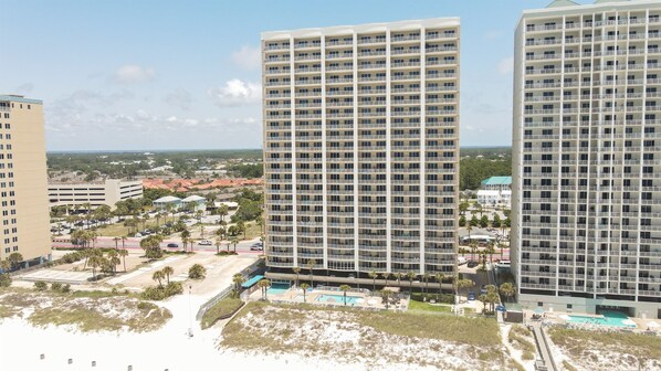 A high-rise hotel with multiple balconies, a swimming pool, and a beach view.