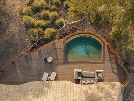 Vista aérea de una piscina privada con cubierta de madera, sillas de descanso y un pequeño rincón de estar.
