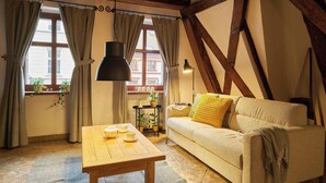 A cozy room with a wooden table, a sofa with cushions, and a window with curtains. - Vincent Old Town Apartments  (Wroclaw)