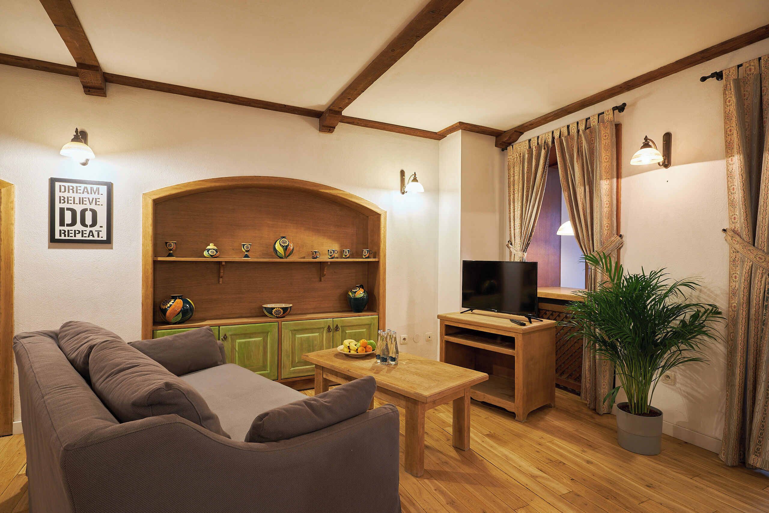 A cozy living room with a wooden bench, a sofa, a television, and a decorative wall with a motivational sign.
