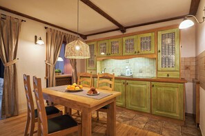 A wooden dining table with chairs, a fruit plate, and a candle. There is a kitchen with green cabinets and a tiled backsplash. - Vincent Old Town Apartments (Wroclaw)