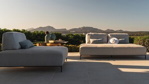 Un área de estar moderna al aire libre con dos sofás y una mesa, con vistas a un paisaje montañoso.