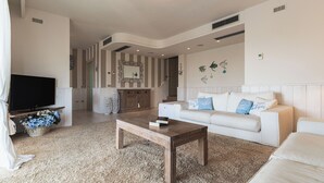 Una sala de estar con una televisión de pantalla plana, una mesa de centro de madera, un sofá blanco y una pared con estampado.