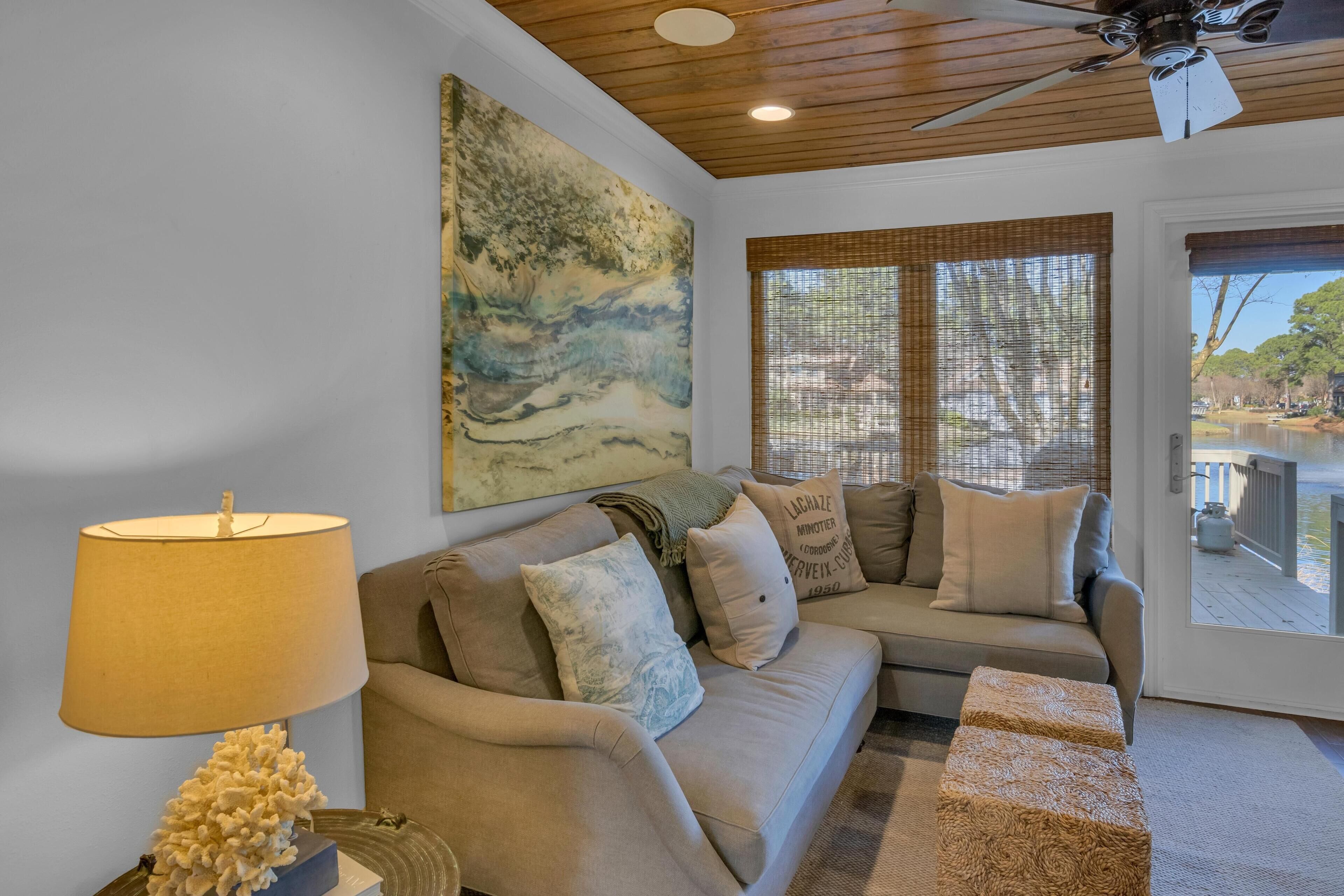 A living room with a beige sofa, a lamp, a painting, and a view of a lake through a window.