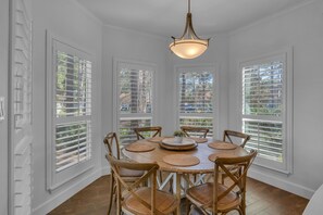Enjoy meals in this cozy dining area with a round table and six chairs, set with a plate, plant, and centerpiece.