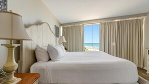 Ein Hotelzimmer mit einem großen Bett, einem Nachttisch aus Holz, einer Lampe und Blick auf den Strand.