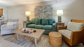 Ein Wohnzimmer mit einem grünen Sofa, zwei Beistelltischen mit Lampen, einem grauen Sessel, einem Couchtisch aus Holz mit Dekorationen und einem Korbsessel.