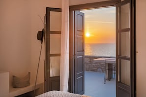 Una puerta abierta que da a un balcón con vistas al mar al atardecer.