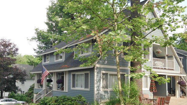 Una casa a due piani con un portico, un piccolo giardino con diverse piante e fiori, e una bandiera americana.