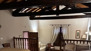 Une chambre à coucher comprenant un lit, une table de chevet, une chaise, une petite table, un canapé et un escalier menant à un autre niveau.