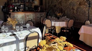Un restaurant aux murs de pierre, aux poutres apparentes et doté d’un bar. Les tables sont dressées avec des nappes blanches et des verres à vin vides.