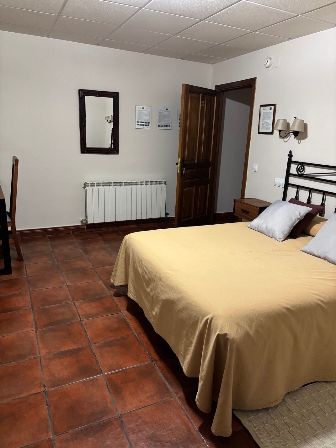 Un dormitorio con cama, radiador, una puerta y una lámpara fijada a la pared.
