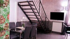 A modern living room with a glass dining table, dark chairs, a staircase, a flat-screen TV, and a radiator. - A un passo dal Castello Maschio Angioino (Naples)
