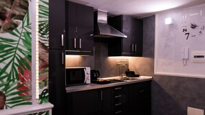 A modern kitchen with dark cabinetry, a stainless steel range hood, a microwave, and a sink. - A un passo dal Castello Maschio Angioino (Naples)