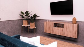 A modern living room with a teal sofa, a wooden cabinet, a flat-screen TV, and two potted plants on a small table. - A un passo dal Castello Maschio Angioino (Naples)