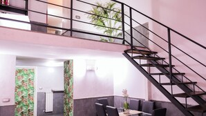 A dining area with a glass table, black chairs, a staircase with a metal railing, and a plant on the upper level. - A un passo dal Castello Maschio Angioino (Naples)