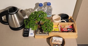 Un plateau avec une bouilloire, des bouteilles d’eau, un petit arbre, des sachets de thé Lipton, des dosettes de café et un souvenir de voyage.