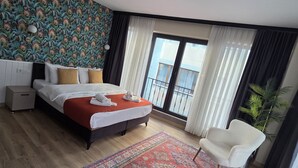 A hotel room with a bed, a nightstand, a chair, a large window with a view, and a patterned rug. - ZULU SUITES (Istanbul)