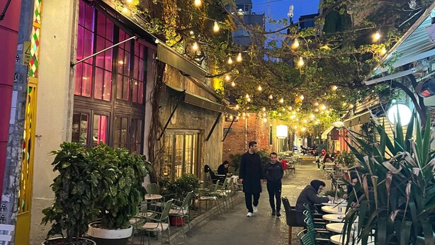 A narrow street lined with outdoor seating areas and potted plants, with string lights overhead. - ZULU SUITES (Istanbul)