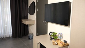 A modern hotel room with a flat-screen TV, a small wooden desk, a coffee maker, and a trash bin. - ZULU SUITES (Istanbul)