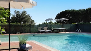 A swimming pool with lounge chairs and umbrellas, surrounded by a fence and greenery. - Sassocupo Apartment (Arezzo)