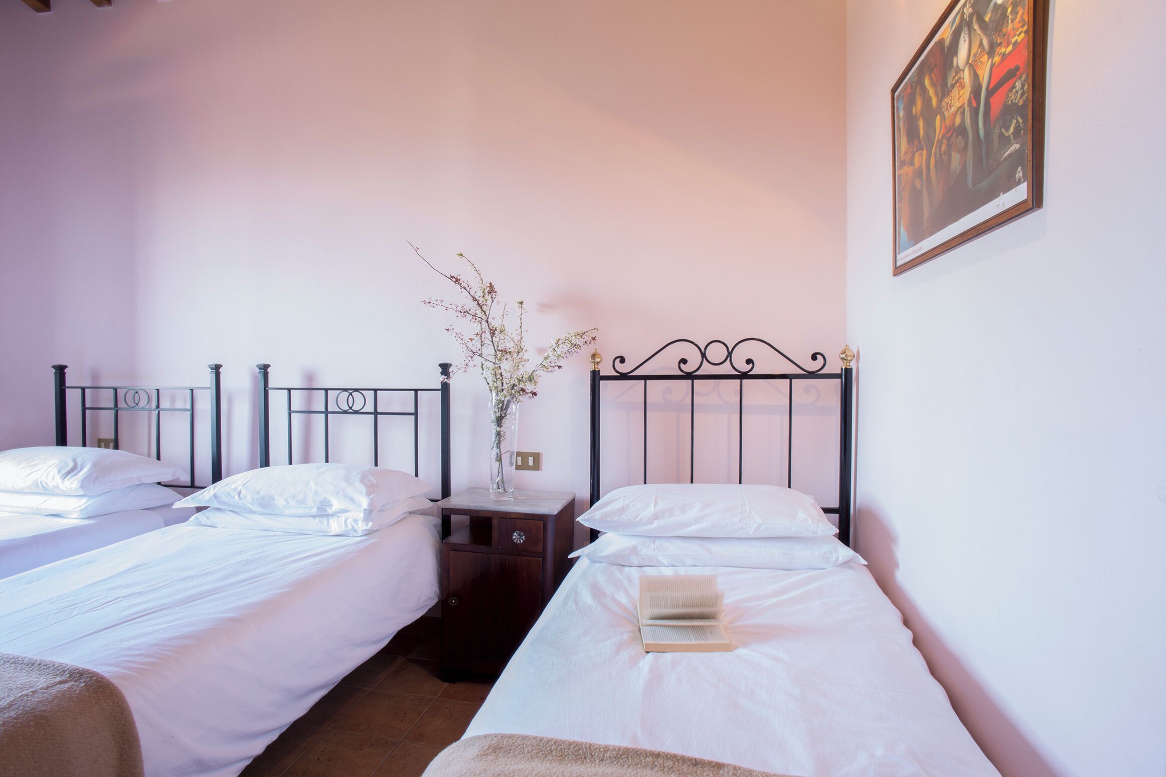 Une chambre avec deux lits simples, une table de chevet ornée d’un vase et un tableau accroché au mur.