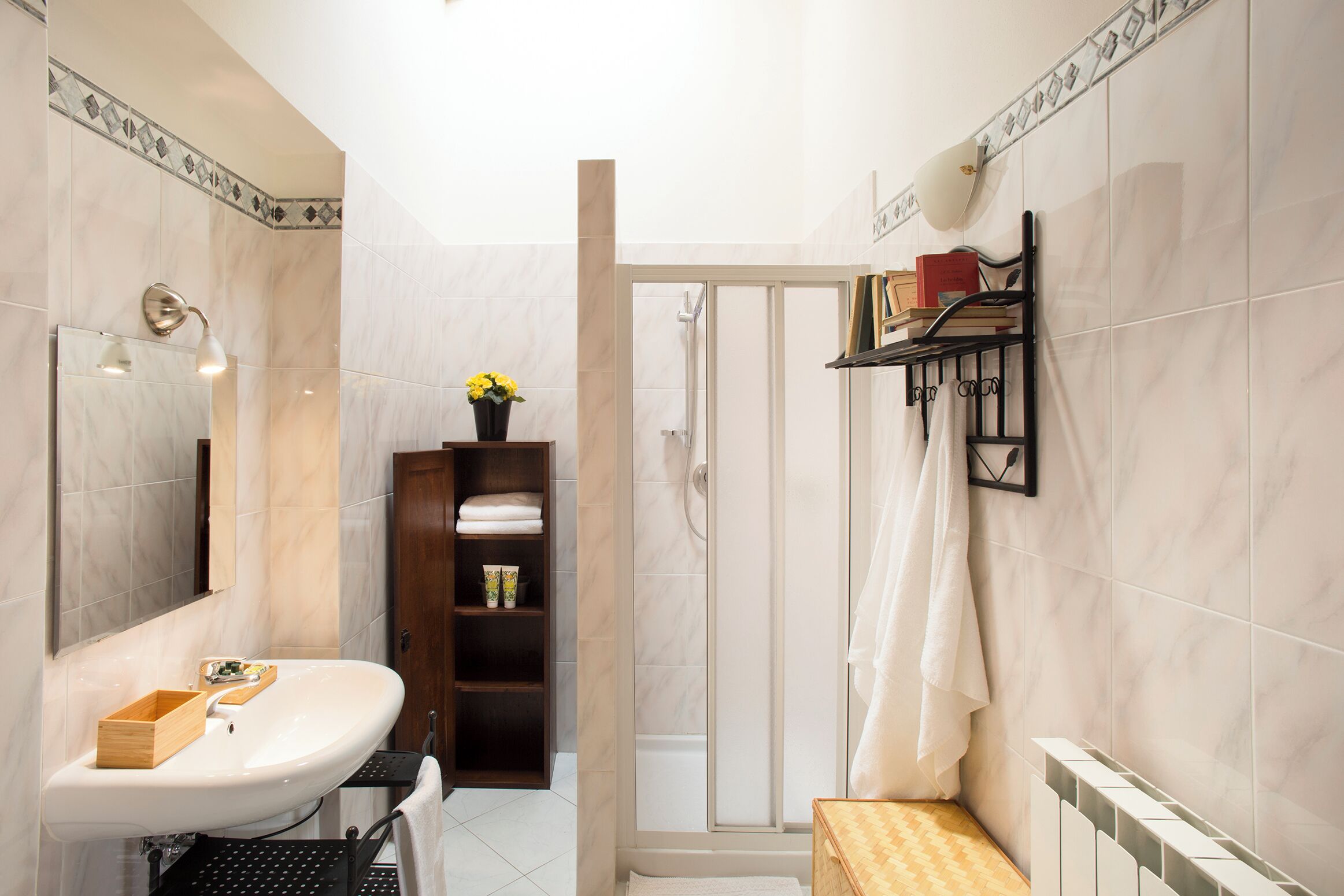 A bathroom with a sink, mirror, shower, and shelves with toiletries.