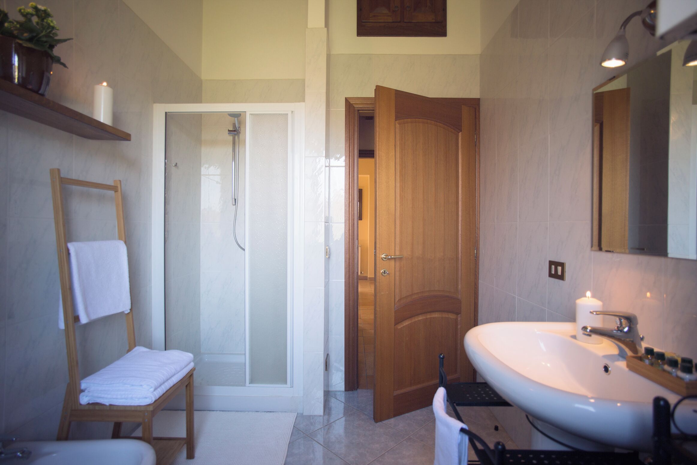 A bathroom with a shower, a sink, a wooden door, and a towel rack.