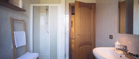 A bathroom with a shower, a sink, a wooden door, and a towel rack.