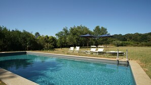 Una piscina rectangular con agua azul cristalina, rodeada de césped con tumbonas y sombrillas.