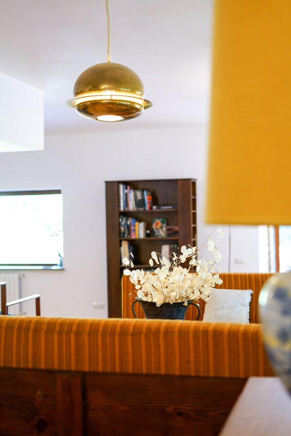 A room with a wooden bench, a hanging brass light fixture, a bookshelf, and a vase with dried flowers.