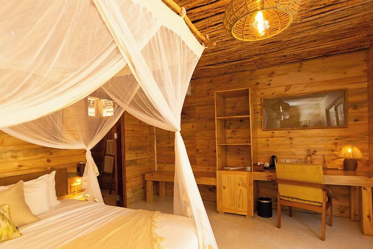 Una habitación de cabaña de madera con una cama bajo un dosel, un escritorio con una silla y un espejo en la pared.