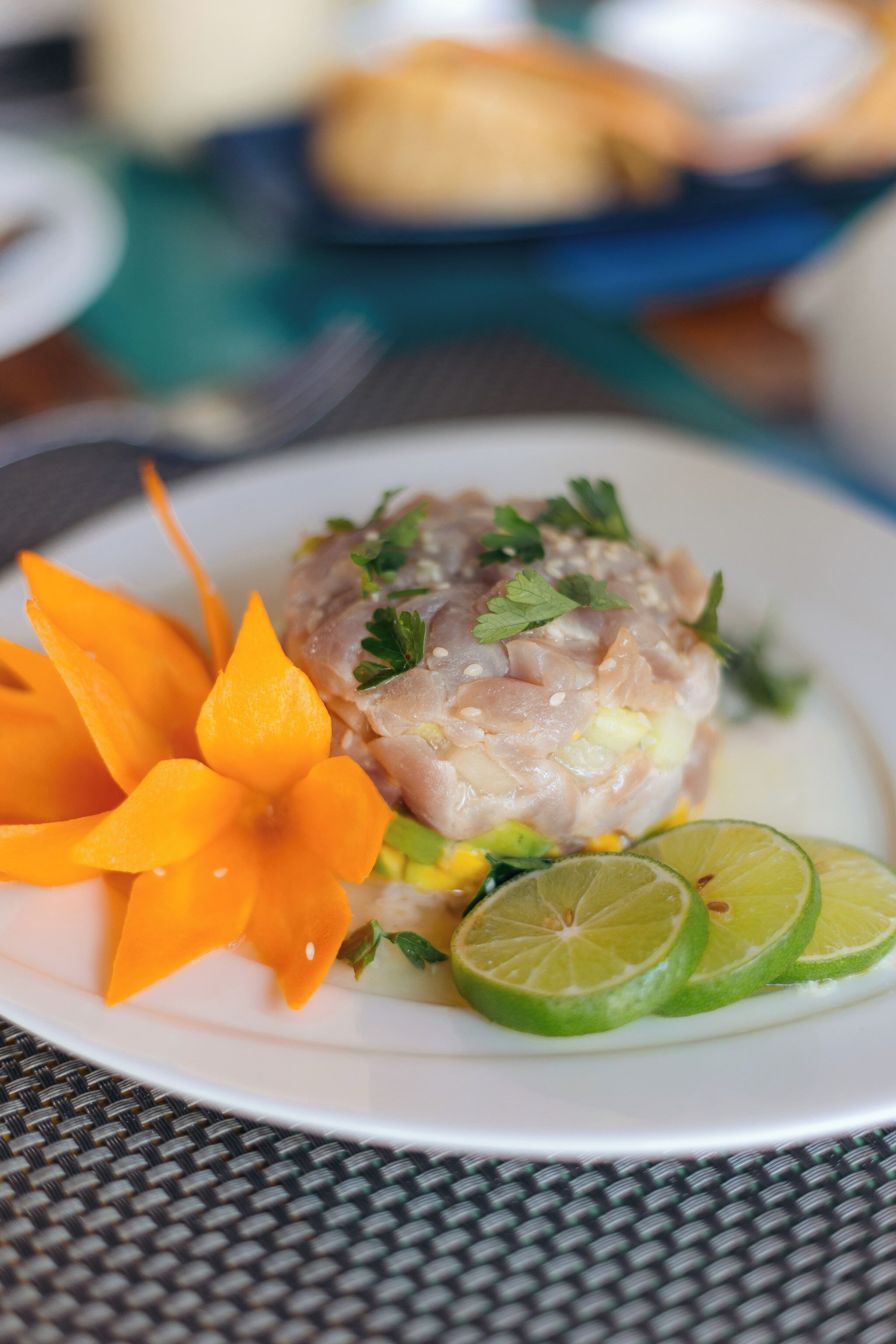 A plate with a dish garnished with parsley, accompanied by carrot slices and lime wedges.