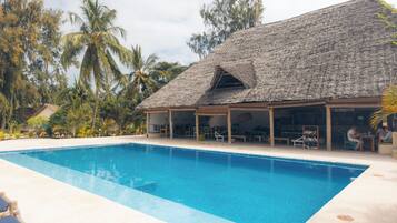 Zona de piscina con una estructura de techo de paja, sillas de descanso y palmeras.