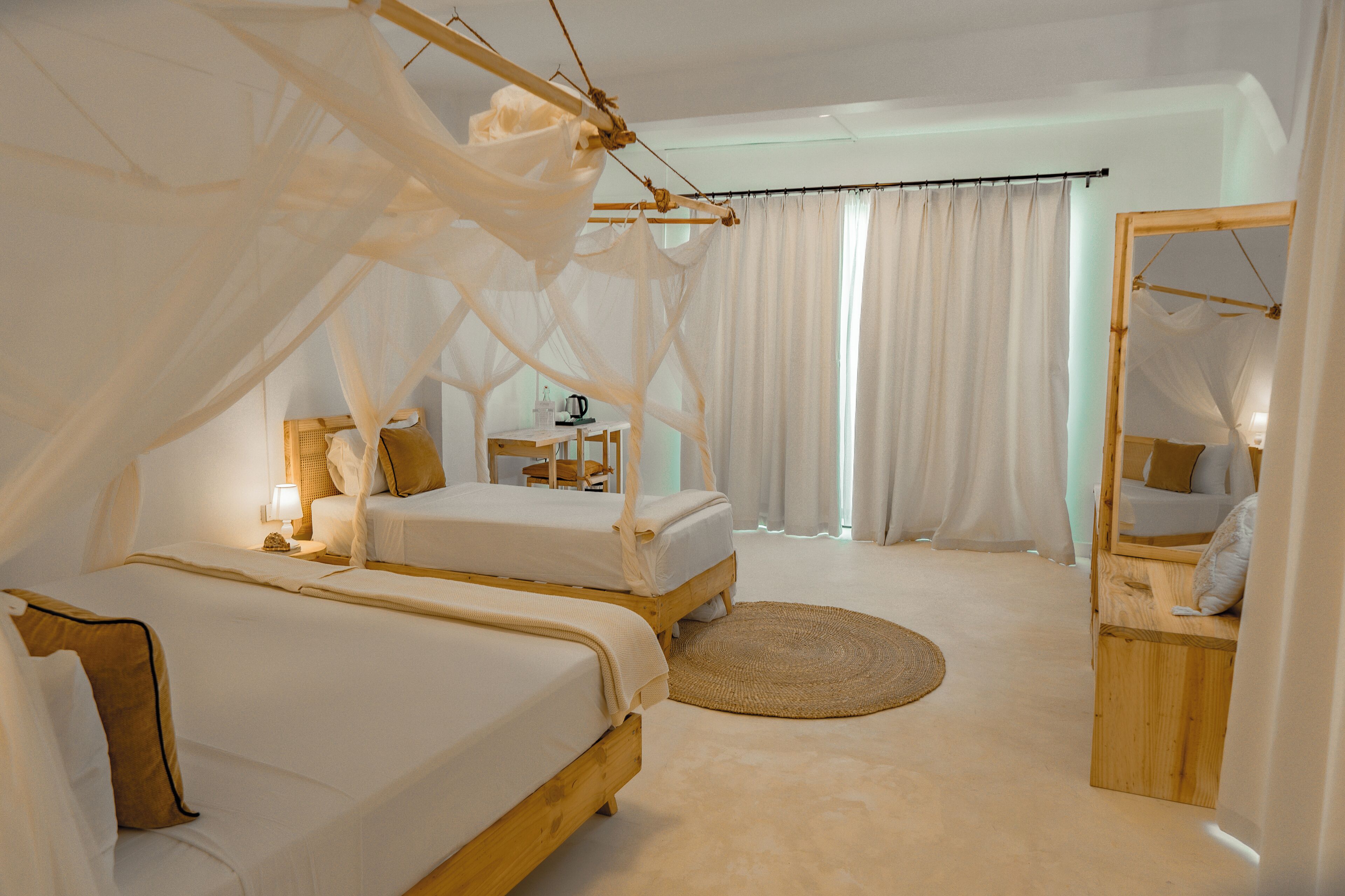 A bedroom with two beds, a wooden headboard, a bedside table with a lamp, and a round rug.