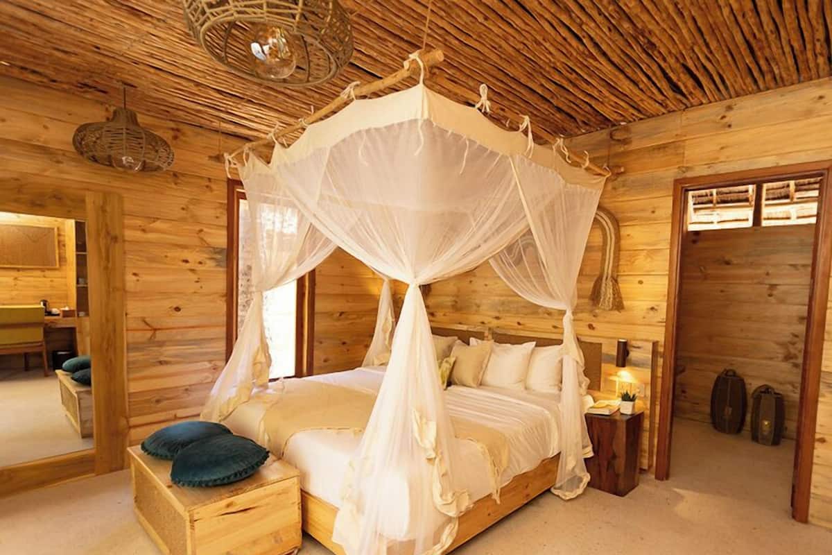 Un dormitorio de cabaña de madera con una cama a cuatro estribos, una mesita de noche pequeña y una mesilla.