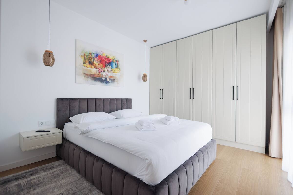 Un dormitorio moderno con una cama grande, una mesita de noche, un armario y un cuadro en la pared.