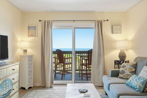 Ein Wohnzimmer mit Fernseher, einer Couch, einem Couchtisch und Meerblick durch eine Schiebetür.