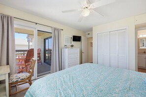A bedroom with a bed, a ceiling fan, a sliding glass door to a balcony, and a TV on the wall.