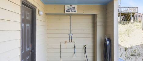 A covered shower area with a sign requesting cleanliness, a door, and a hose.
